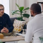 Man, patient or talking to psychologist on sofa in mental health, depression or anxiety counselling therapy. Psychology, stress or wellness counseling therapy help for person in rehabilitation clinic